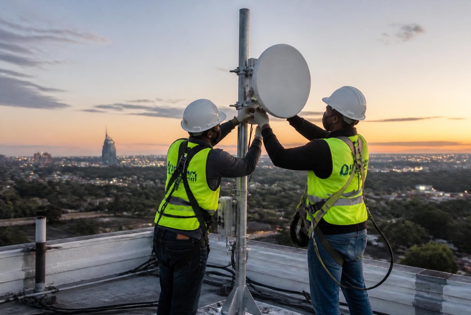 CKPK engineers aligning a wireless backhaul dish on a rooftop at dusk